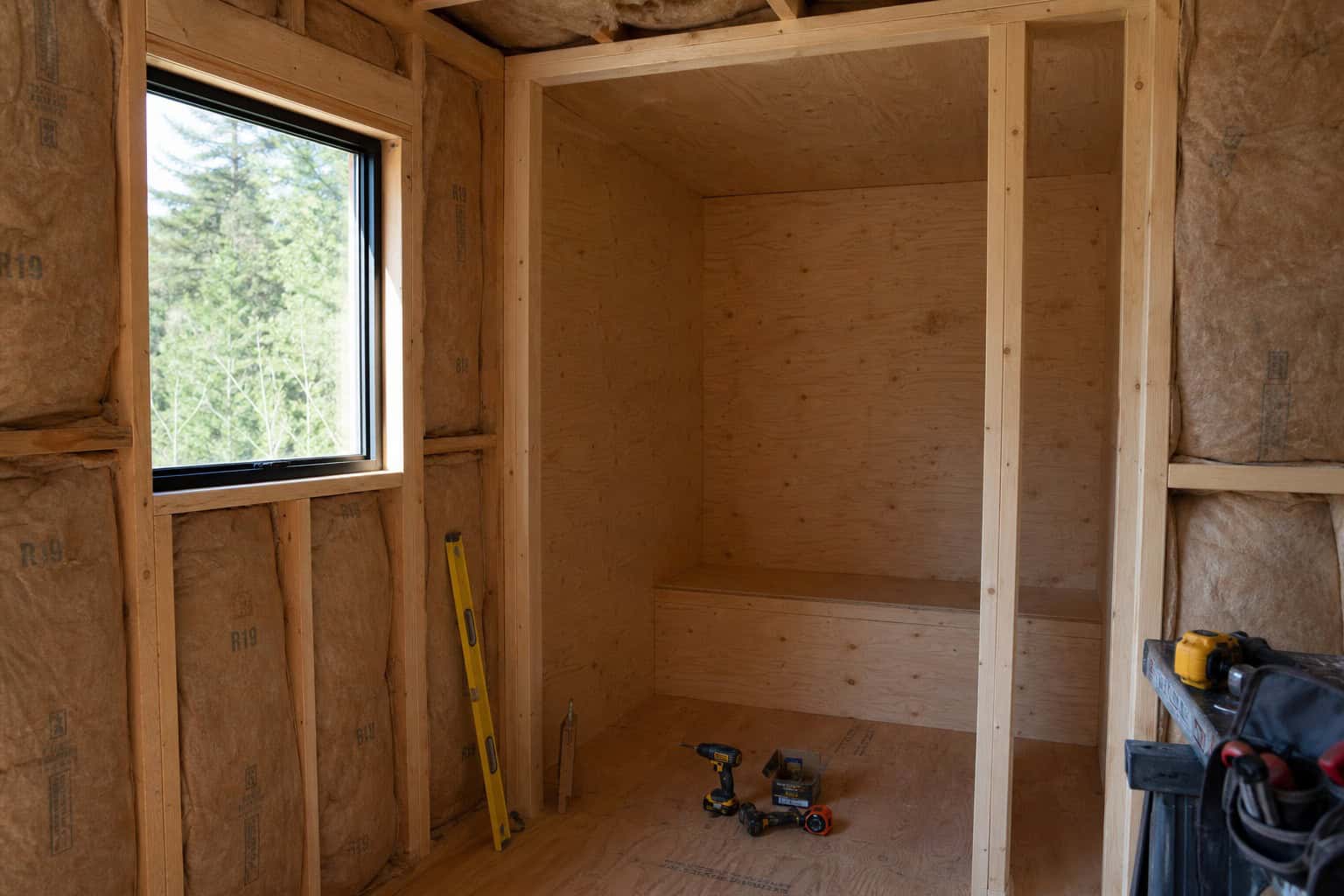 DIY sauna frame under construction with 2x4 studs and plywood, showing the building process.